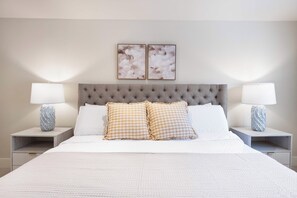 Ein ordentlich bezogenes Bett mit einem karierten Kopfkissen, zwei Nachttischlampen und zwei gerahmten Bildern an der Wand.