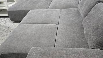 A grey sectional sofa with a matching ottoman in a room with a white wall and a small white side table.