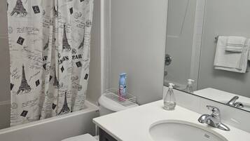 A bathroom with a shower curtain featuring the Eiffel Tower, a white toilet, a sink with a mirror, and a towel rack.