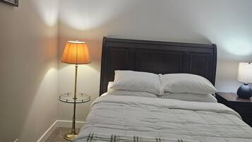 A neatly made bed with a plaid blanket, a bedside lamp, and a dark headboard in a room with plain walls.