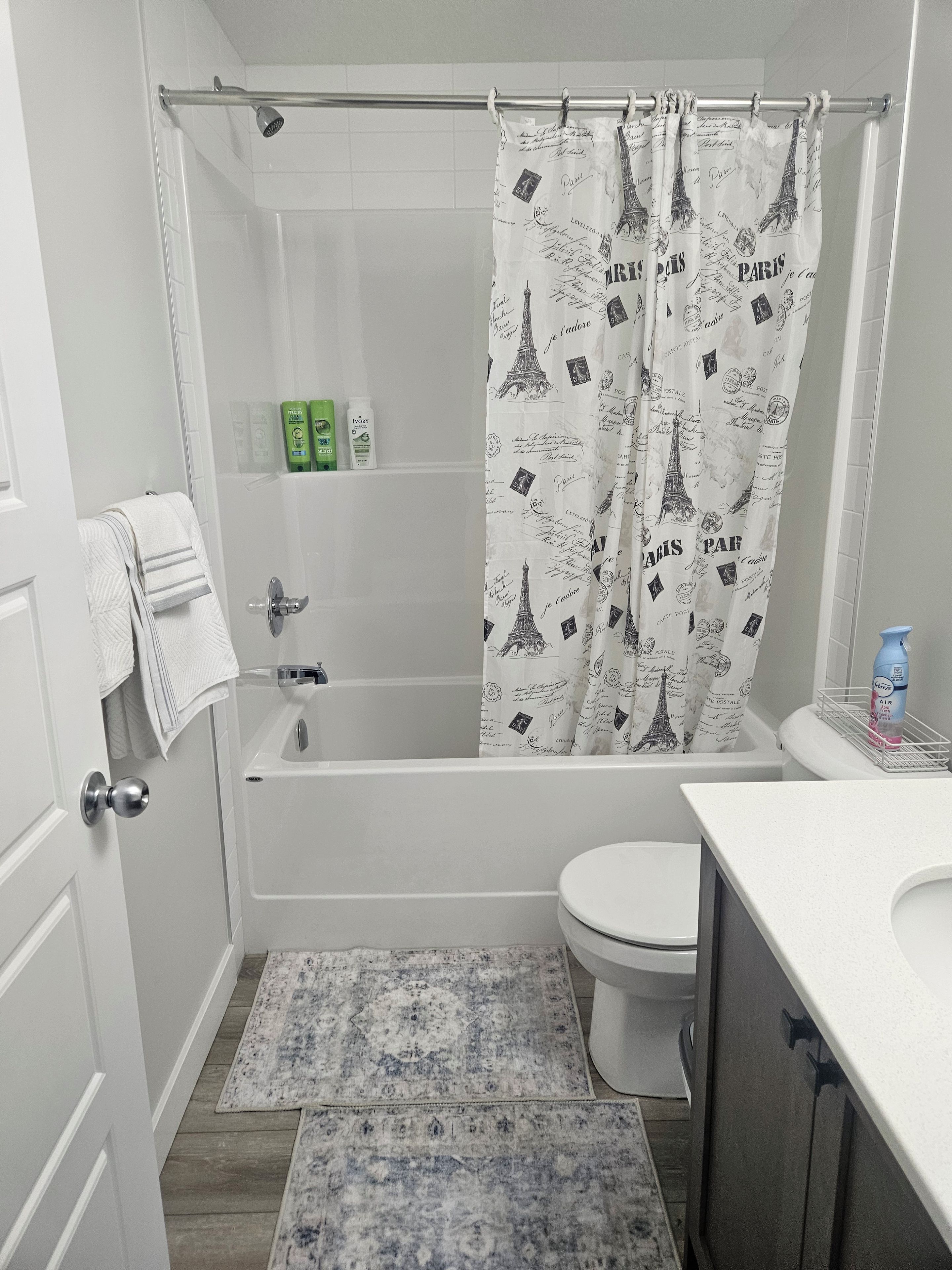 A bathroom with a shower curtain featuring the Eiffel Tower, a bathtub, a toilet, and a sink with toiletries.