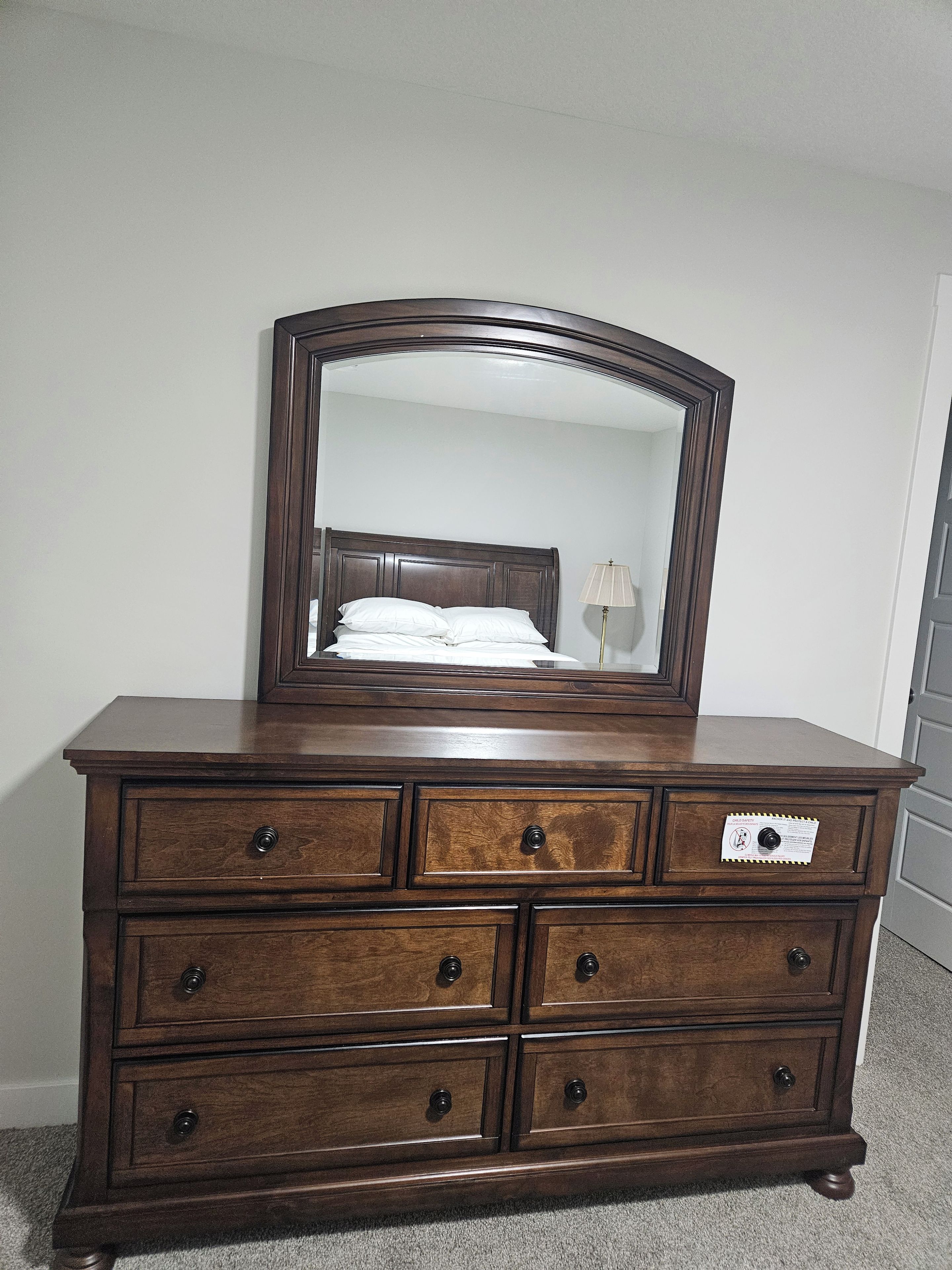 A wooden dresser with a mirror, drawers, and a bed in the background.
