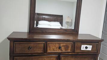 A wooden dresser with a mirror, drawers, and a bed in the background.