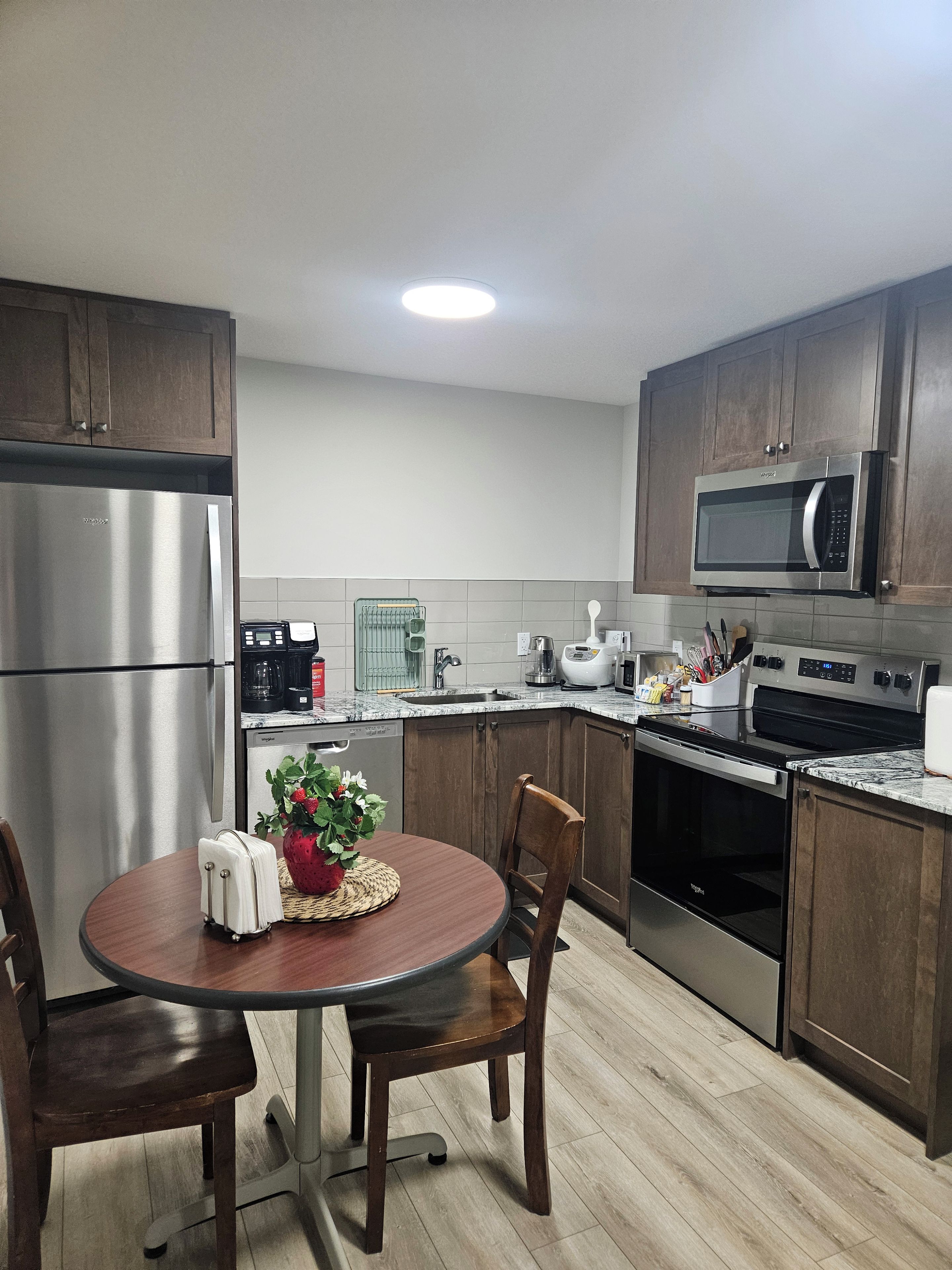 A modern kitchen with stainless steel appliances, wooden cabinets, and a dining area with a round table and chairs.