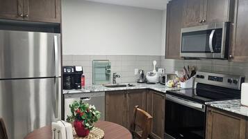 A modern kitchen with stainless steel appliances, wooden cabinets, and a dining area with a round table and chairs.