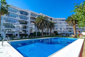 Ein modernes Hotel mit Schwimmbad, mehreren Balkonen und Palmen.