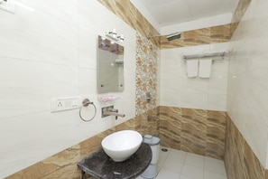 Een badkamer met een wit wastafelmeubel, een spiegel, een handdoekhouder en een douchegedeelte.