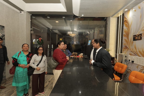 A reception area with a black counter, a man in a suit, and several people standing. - Hotel A.P. Palace (Agra)