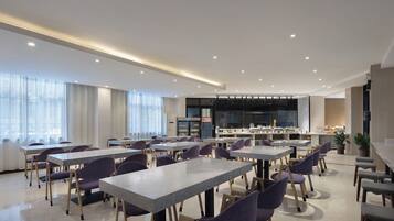 A modern dining area with multiple tables and chairs, a kitchen area with appliances, and a large screen for presentations.