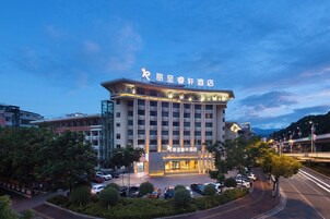 Un hotel con fachada moderna, varios pisos y un estacionamiento con varios automóviles.