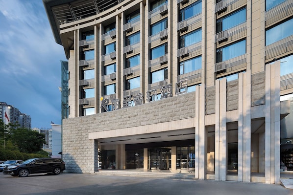 Un hotel moderno con una entrada destacada, varios pisos y un cielo despejado.
