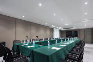 Un salón de conferencias con una larga mesa, sillas, micrófonos y botellas de agua.