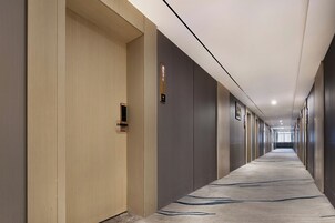 A long, narrow hotel corridor with a carpeted floor, wooden and grey walls, and a series of doors on one side.