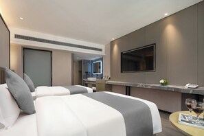 A hotel room with two beds, a TV, a minibar, and a small table with glasses.