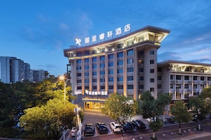 Un hotel de varios pisos con un letrero llamativo en la parte superior, un estacionamiento con varios automóviles y zonas verdes circundantes.