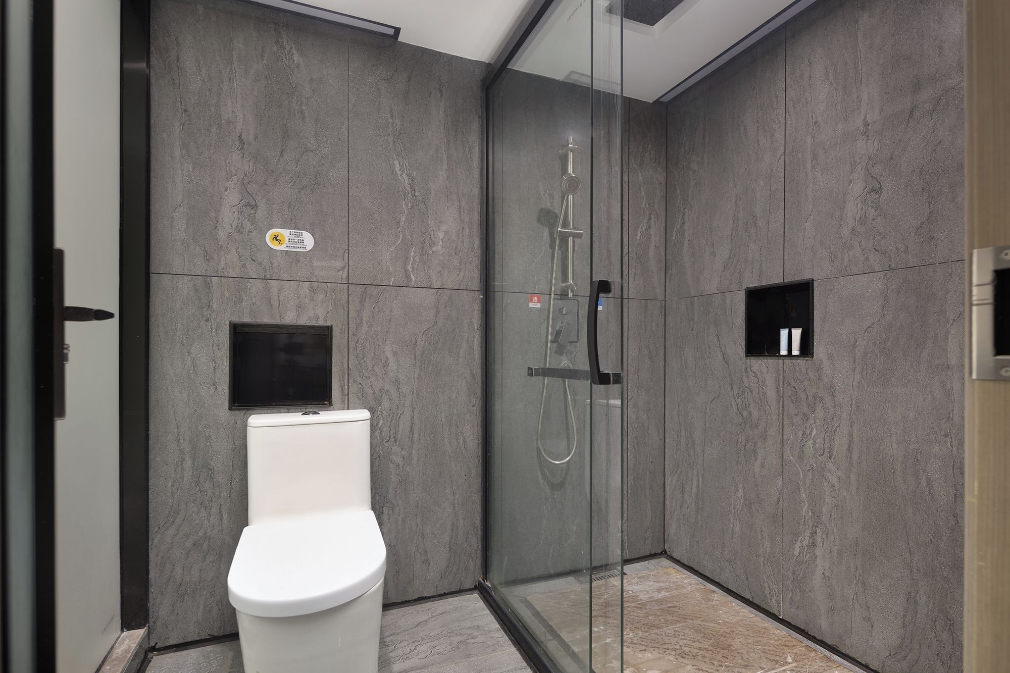 A modern bathroom with a glass-enclosed shower, a toilet, and a small shelf with toiletries.