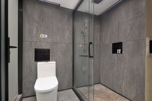 Un baño moderno con ducha de vidrio, inodoro y un pequeño estante con artículos de aseo.