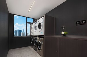 A modern laundry room with two washing machines, a large window with a city view, and a sign indicating the location.