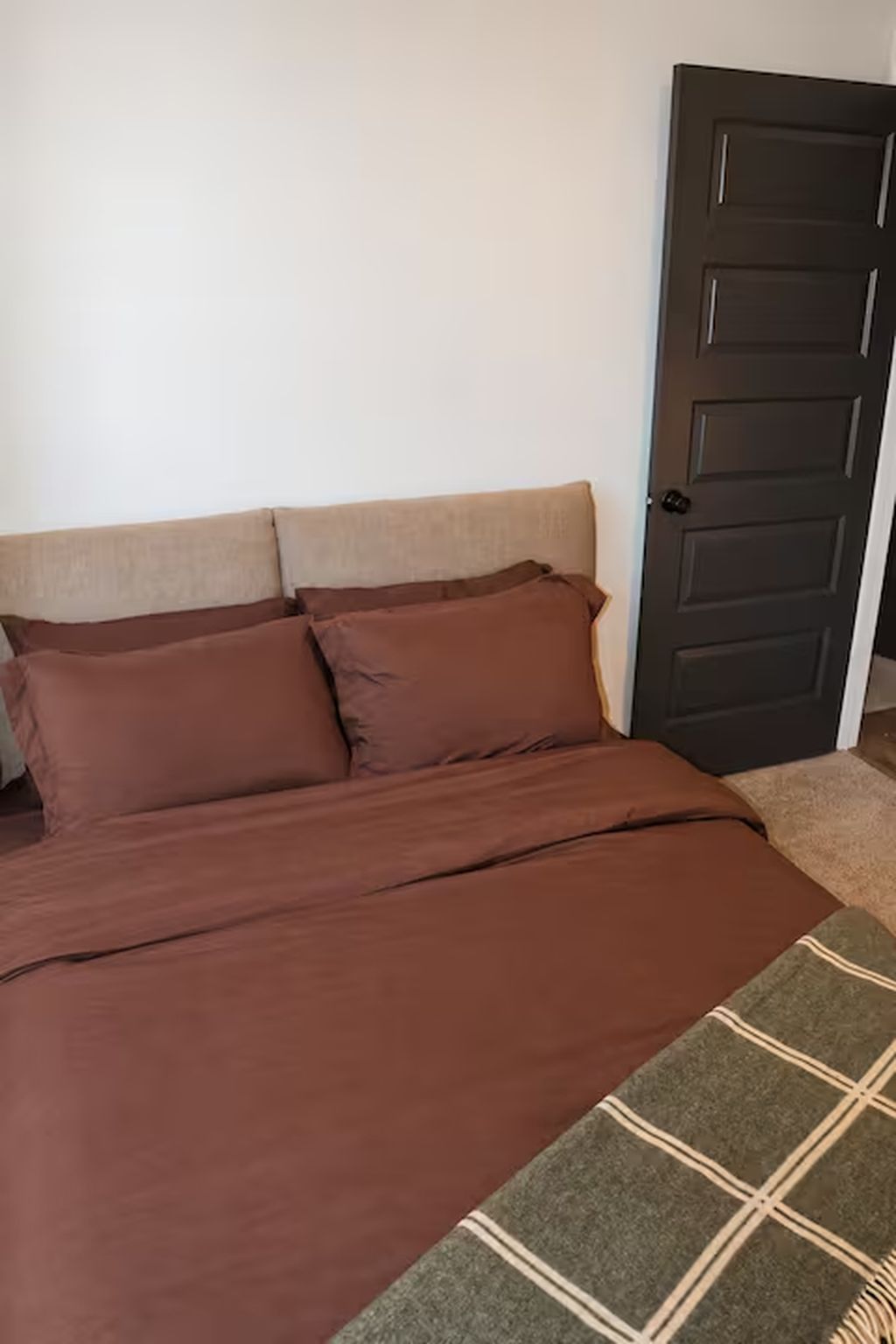 A bed with a brown bedspread and two pillows, a door to the right, and a partial view of a patterned rug.