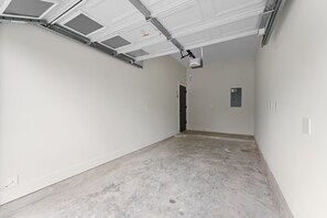 A clean, empty hallway with white walls, a concrete floor, and a garage door with a ceiling fan. - Entire duplex | Two homes, one stay (Houston)