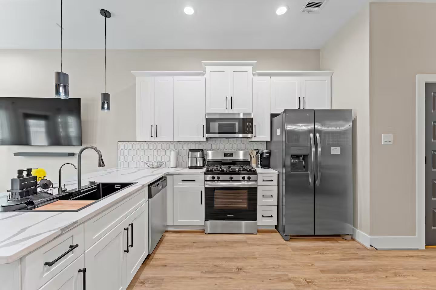 Una cocina moderna con armarios blancos, electrodomésticos de acero inoxidable, horno empotrado y un refrigerador grande.