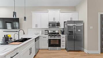 Una cocina moderna con armarios blancos, electrodomésticos de acero inoxidable, horno empotrado y un refrigerador grande.