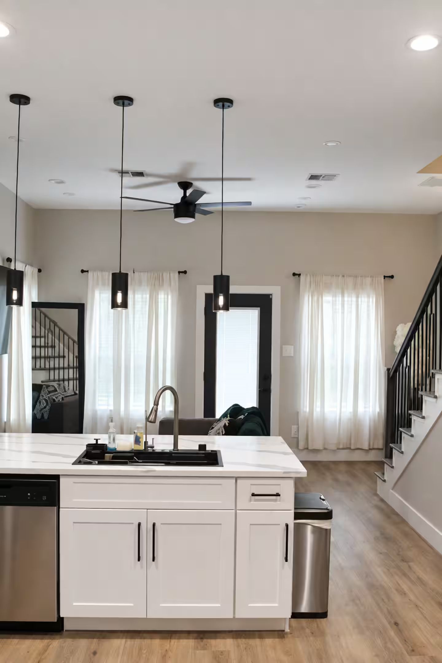 A modern kitchen with a central island, pendant lights, a ceiling fan, and a stainless steel dishwasher.