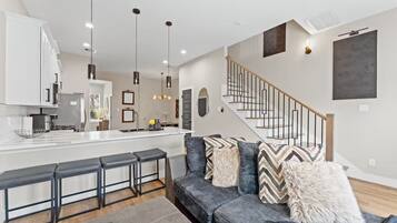 A modern kitchen with a central island, bar stools, and pendant lighting.