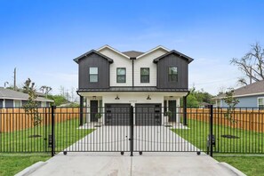 A two-story residential house with a front garage, a black metal fence, and a well-maintained lawn. - Entire duplex | Two homes, one stay (Houston)