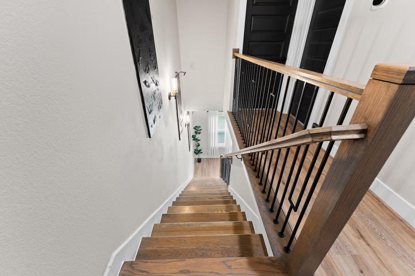 A wooden staircase with a handrail, white walls, and a black door at the top.