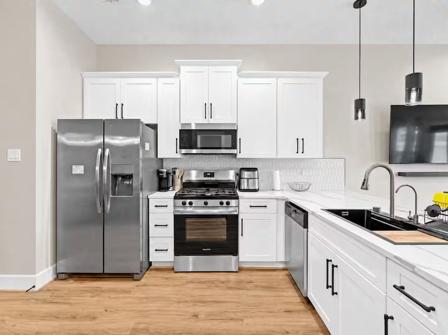 A modern kitchen with white cabinets, stainless steel appliances, and a wooden floor.