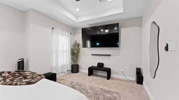 A modern bedroom with a large bed, a TV mounted on the wall, a potted plant, and a bench.