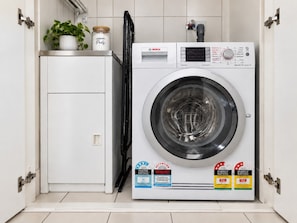 A compact, white washing machine with a digital display, energy and water rating labels, and a small potted plant on top. - Melbourne Paws Escape | Pool, Gym & Sauna (Melbourne)