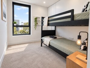 A bunk bed room with a window, a bedside table with a lamp, and a small plant. - Melbourne Paws Escape | Pool, Gym & Sauna (Melbourne)