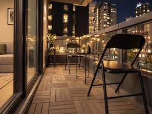 A balcony with a wooden floor, two chairs, a small table, and a potted plant. - Melbourne Paws Escape | Pool, Gym & Sauna (Melbourne)