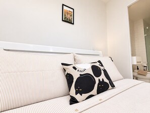 A bed with striped bedding, a framed picture on the wall, and a bathroom visible through an open door. - Melbourne Paws Escape | Pool, Gym & Sauna (Melbourne)