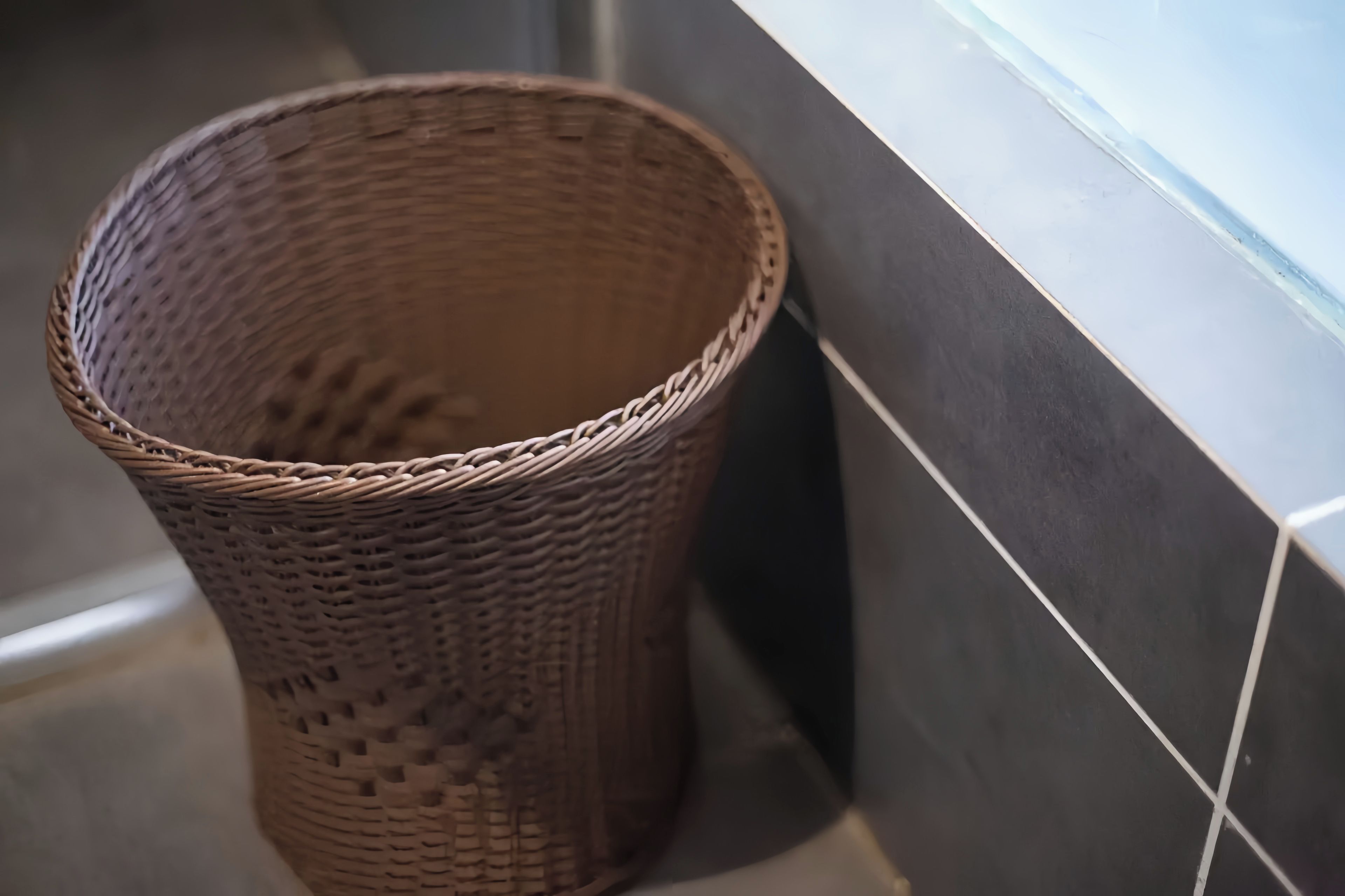 A wicker basket placed against a tiled wall.