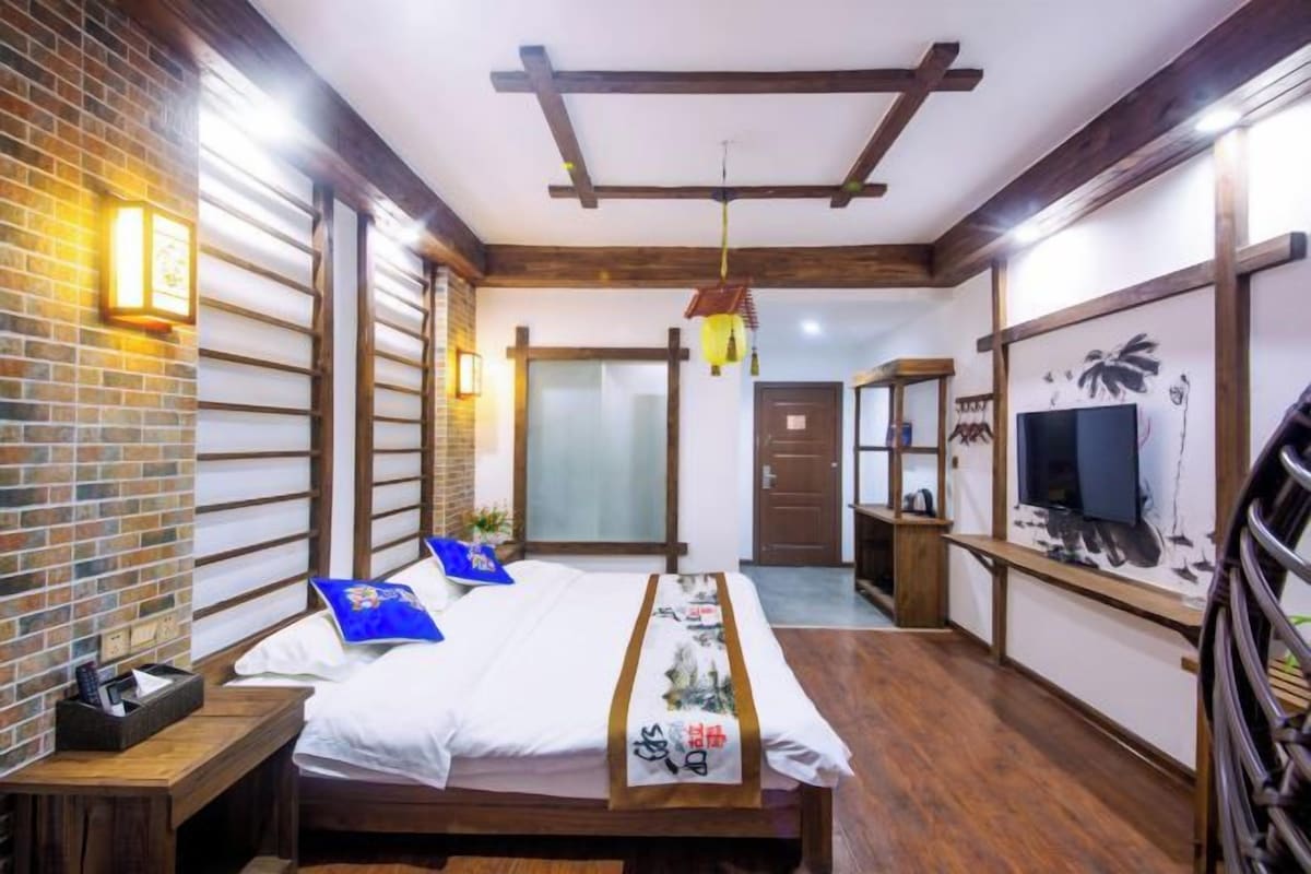 A hotel room with a bed, a TV, a wooden bench, and a brick wall.