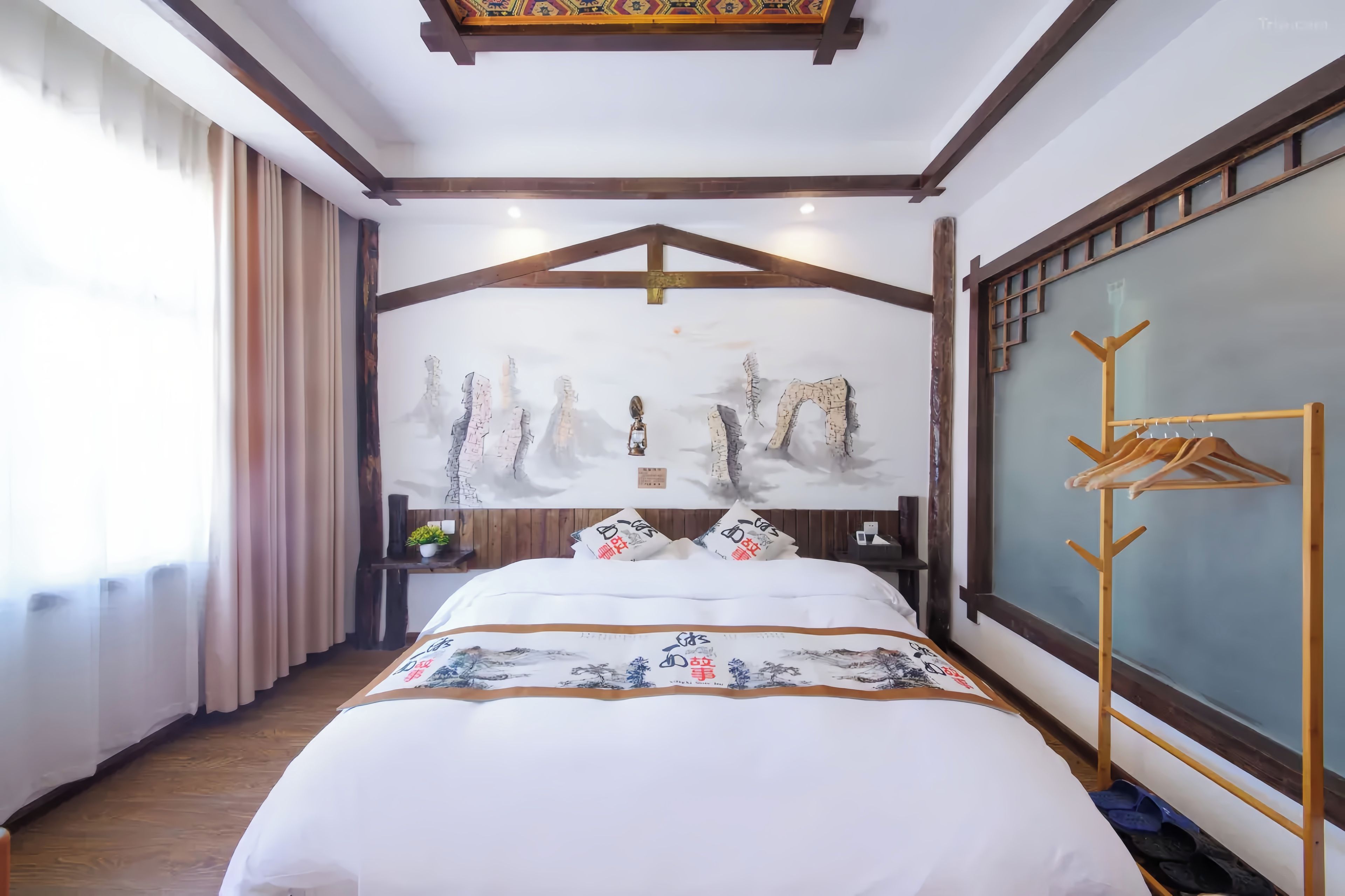 A hotel room with a bed, a wooden headboard, a wall-mounted coat rack, and a window with curtains.