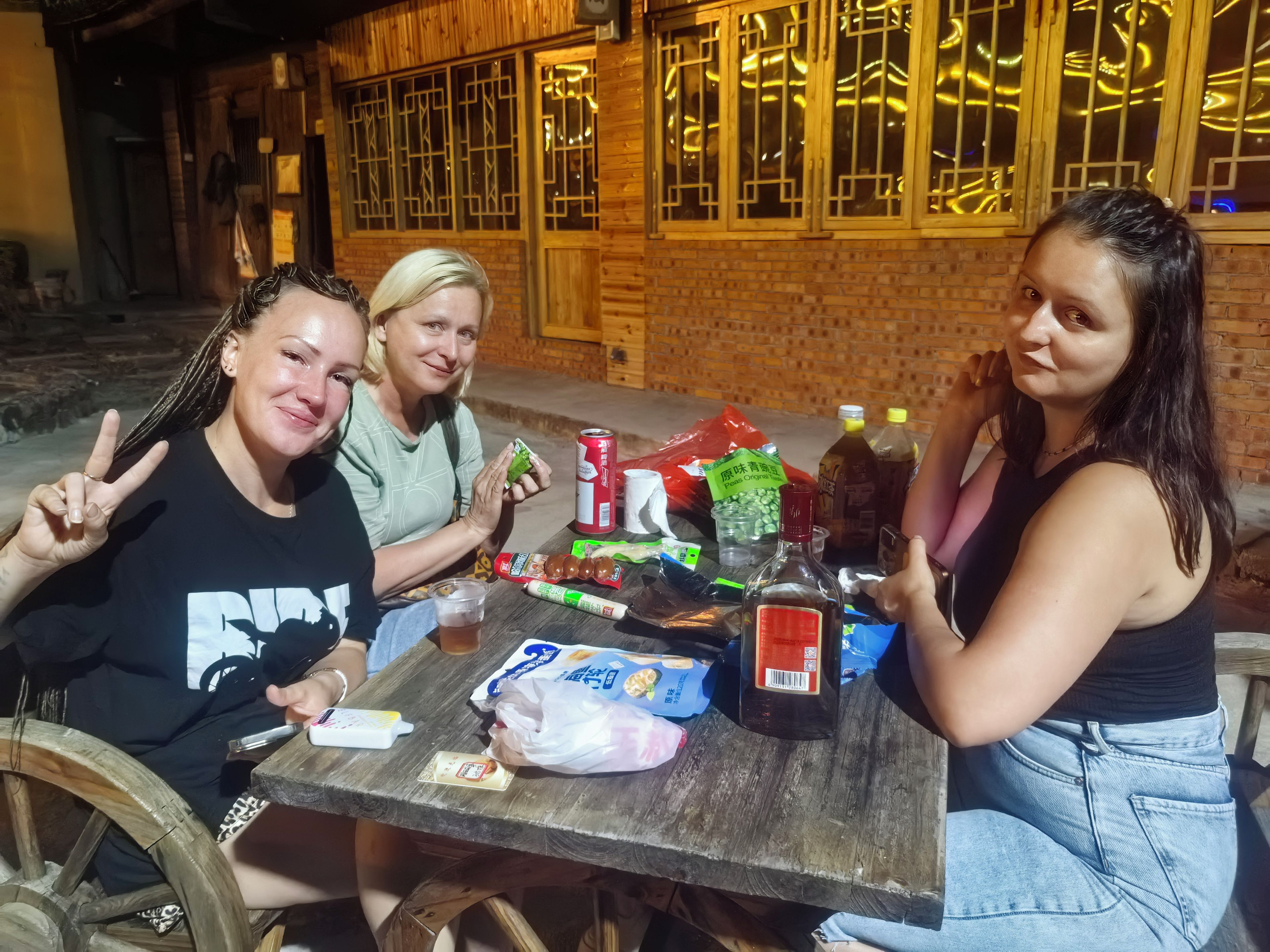 Tres personas sentadas en una mesa al aire libre, con diferentes comidas y bebidas.