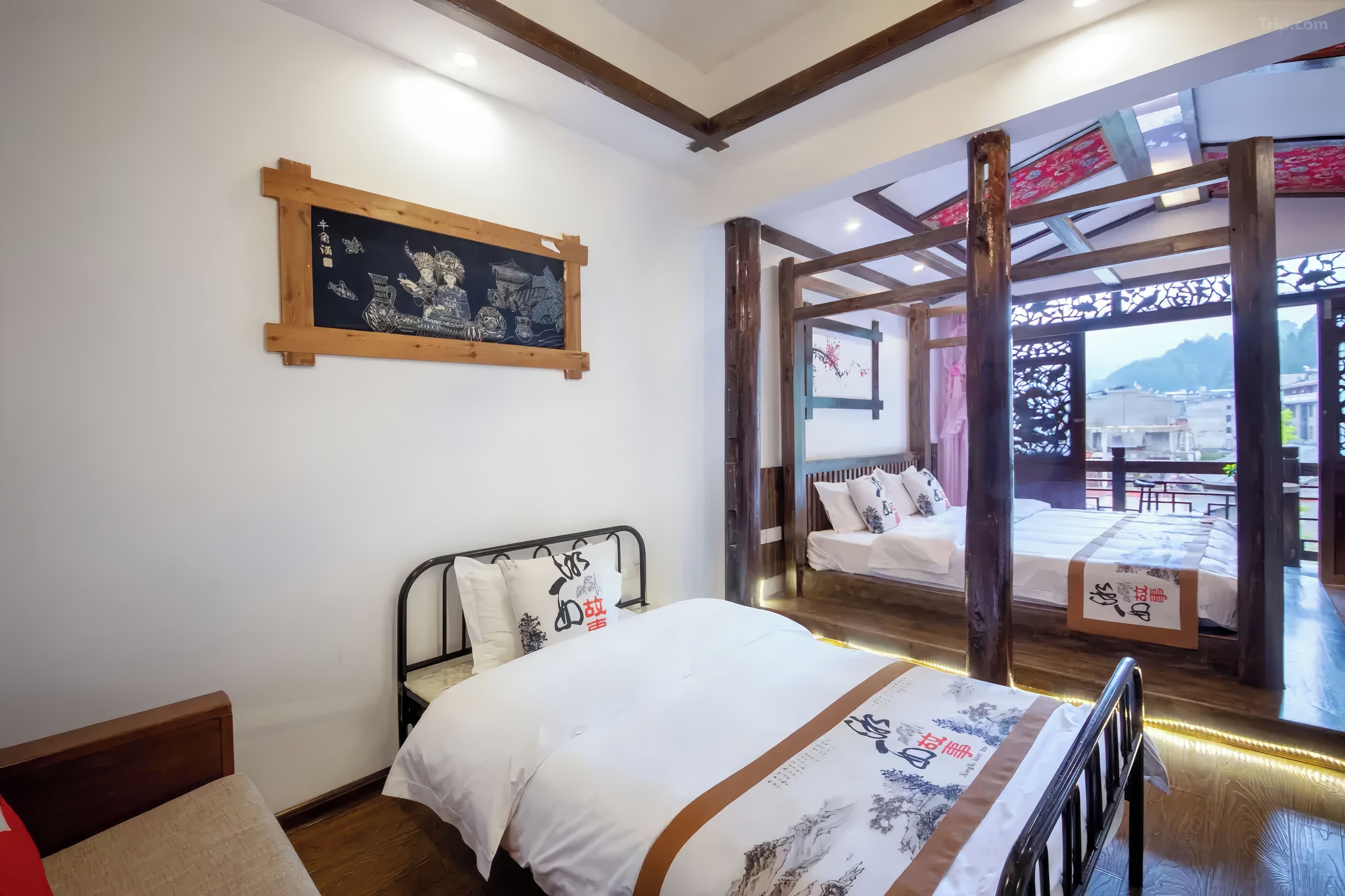 A hotel room with a bed, a wooden headboard, a wall-mounted artwork, and a balcony with a view.