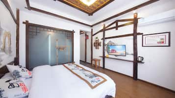 Quarto de hotel com cama, escrivaninha, televisão e prateleira fixada na parede.