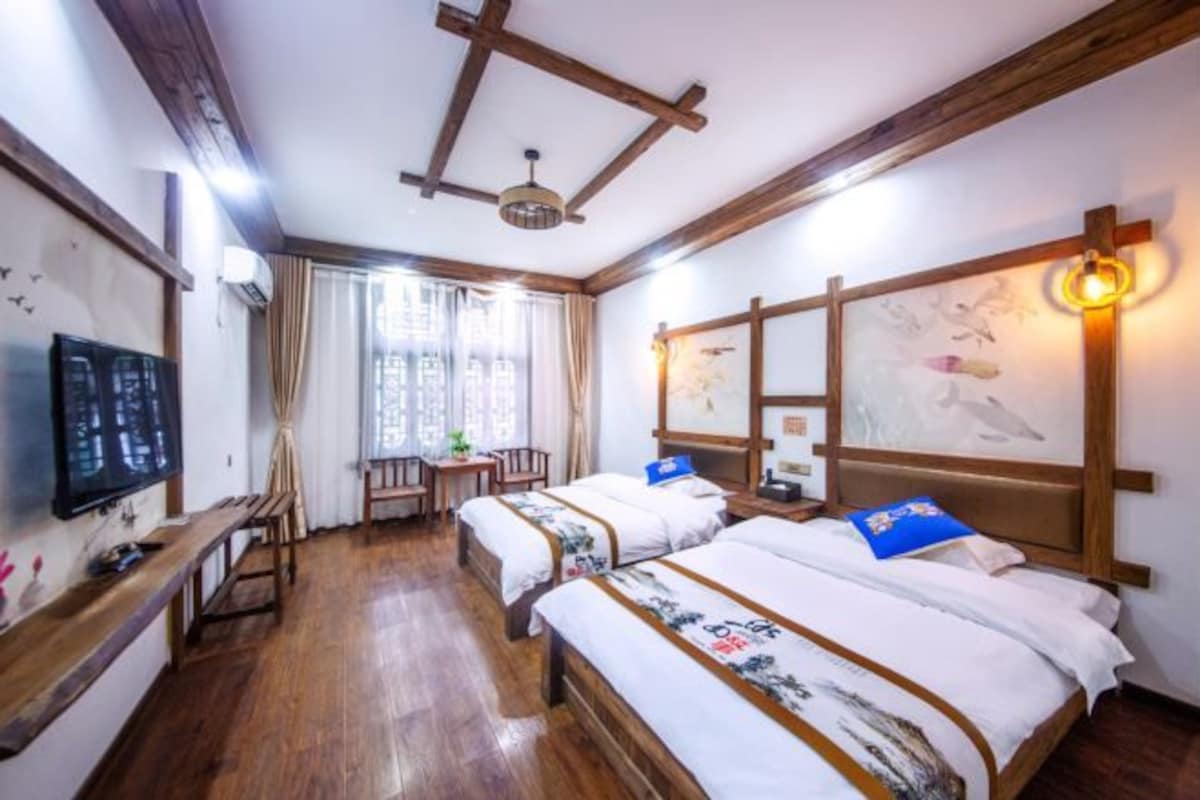 A hotel room with wooden beams, two beds with floral bedding, a desk, a chair, and a TV.