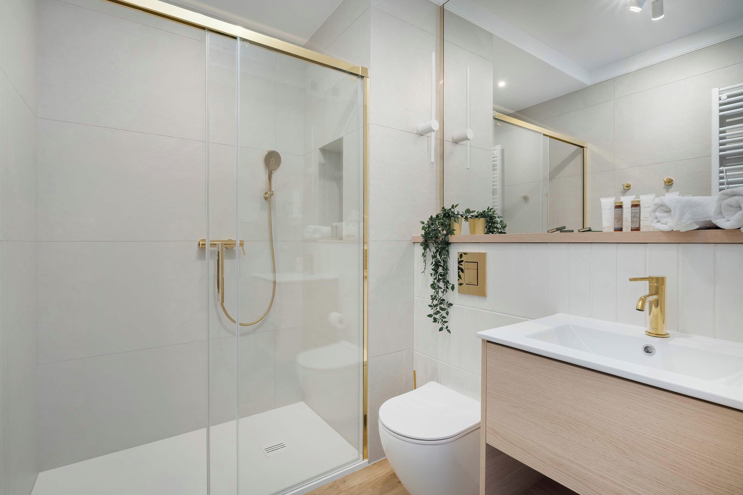Une salle de bain moderne avec une douche à parois de verre, des toilettes blanches et un meuble-lavabo doté d’un robinet doré.