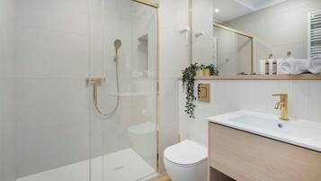 Une salle de bain moderne avec une douche à parois de verre, des toilettes blanches et un meuble-lavabo doté d’un robinet doré.