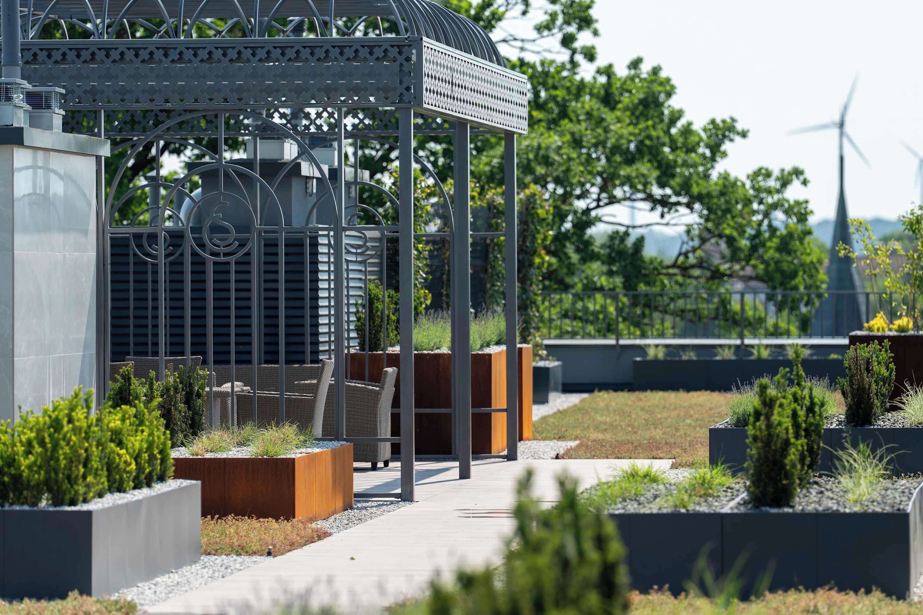 A modern outdoor area with a metal gazebo, seating, planters, and a pathway.