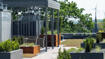 A modern outdoor area with a metal gazebo, seating, planters, and a pathway.