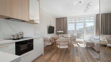 Eine moderne Küche mit Backofen, ein Essbereich mit Tisch und Stühlen sowie ein Wohnzimmer mit Sofa und Blick auf die Stadt.