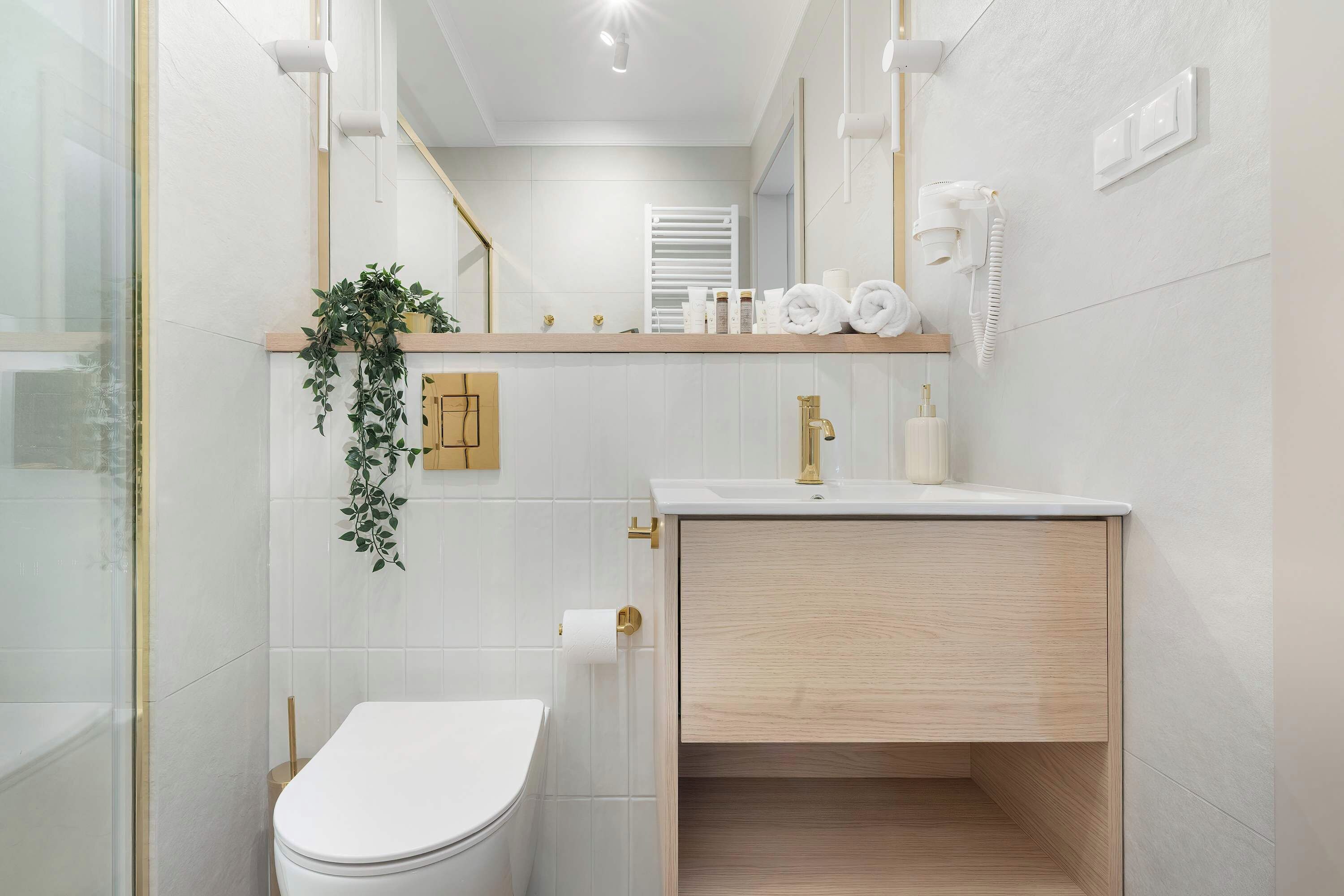 A bathroom with a toilet, sink, and mirror. There is a plant on the wall and toiletries on the counter.