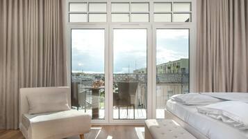 Une chambre dotée d’une grande porte-fenêtre coulissante donnant sur un balcon, avec un lit, une chaise et une vue sur les immeubles.